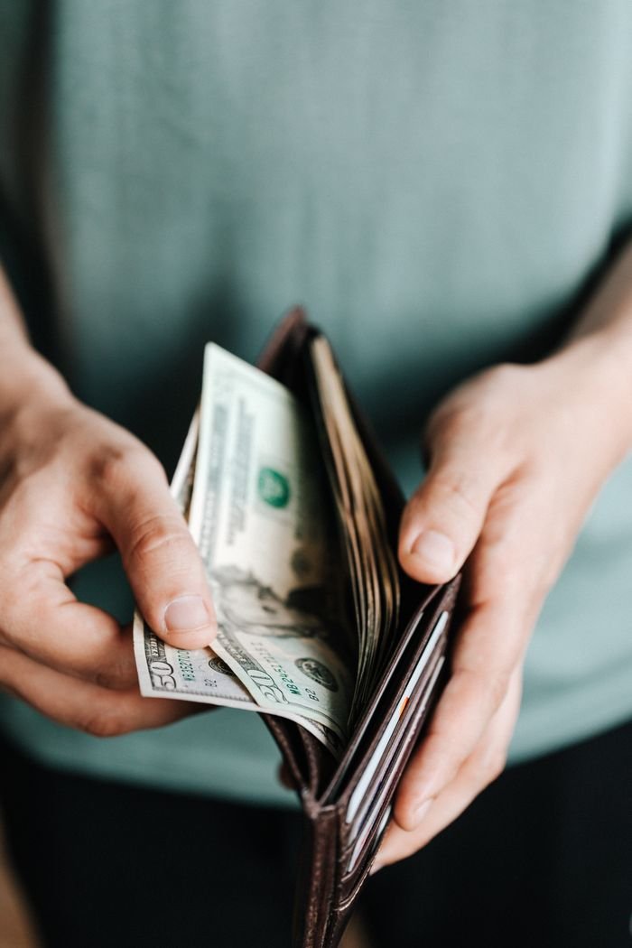 From above of crop unrecognizable man in casual outfit holding wallet with banknotes getting dollars up