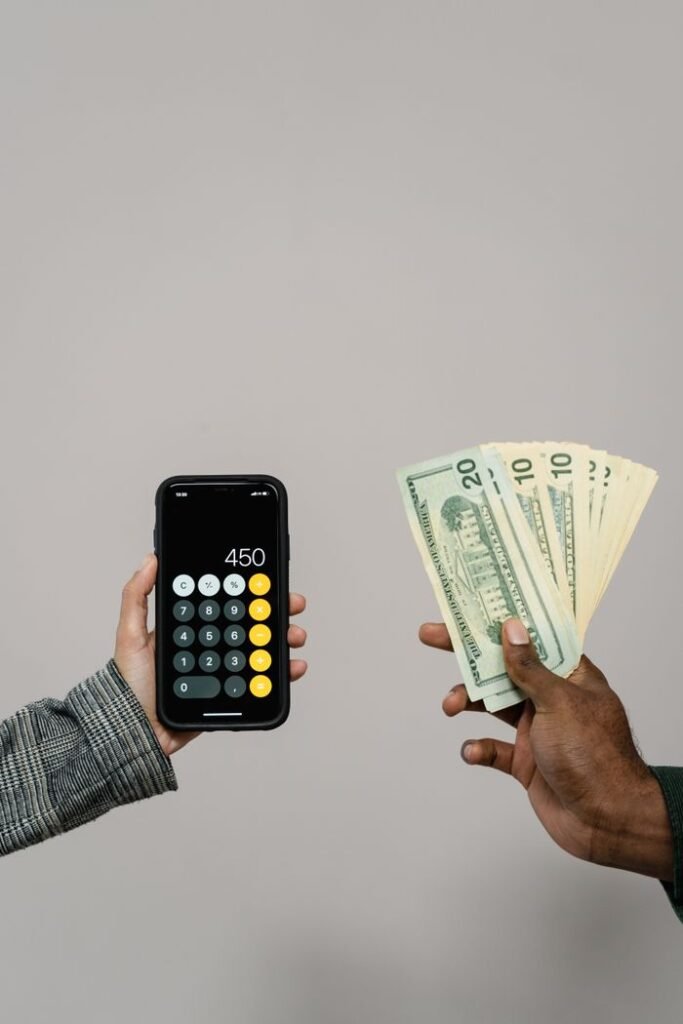 Hands exchanging cash and using a calculator on a smartphone against a gray background.
