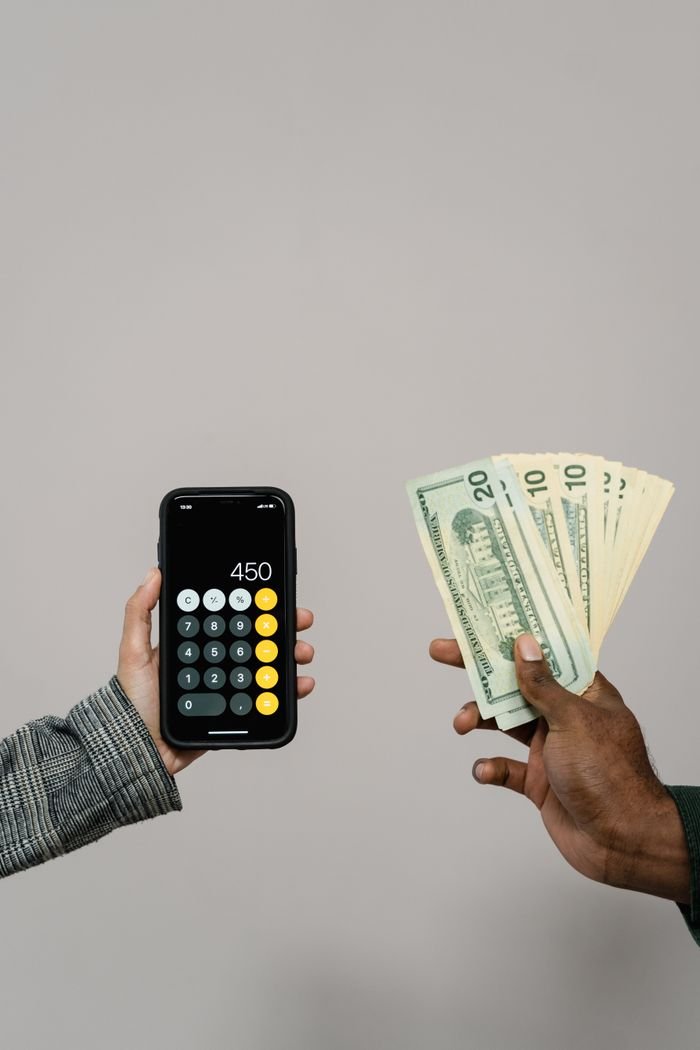 Hands exchanging cash and using a calculator on a smartphone against a gray background.